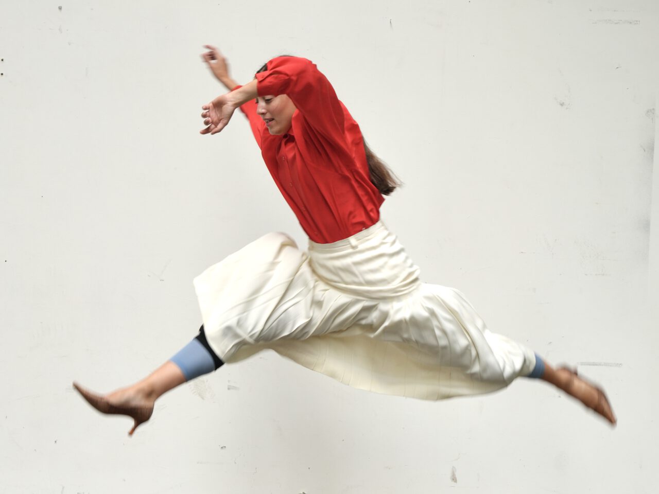 A dancer leaps dynamically through the air, wearing a red top and a flowing white skirt.