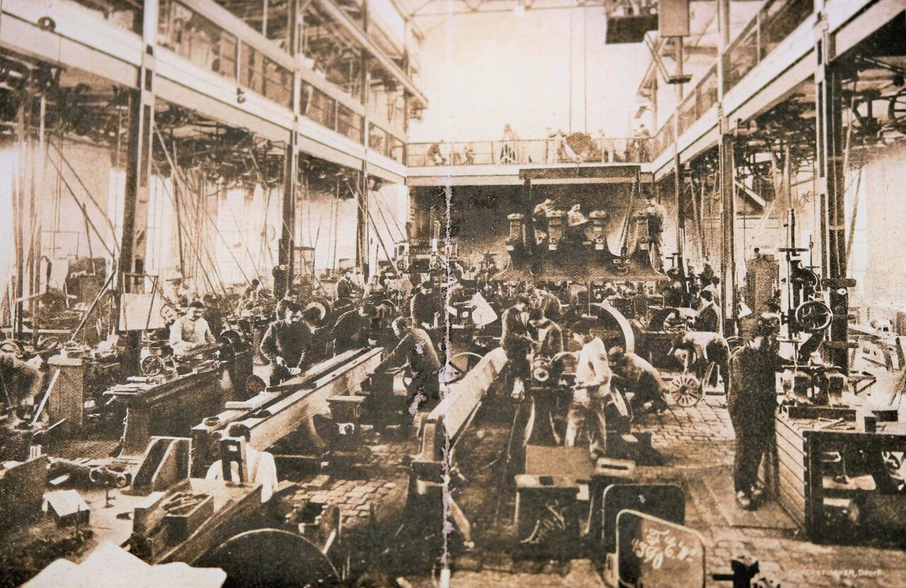 Historische Aufnahme einer großen Werkhalle der Naxos-Union um 1900, mit zahlreichen Arbeitern an Maschinen und Werkbänken.