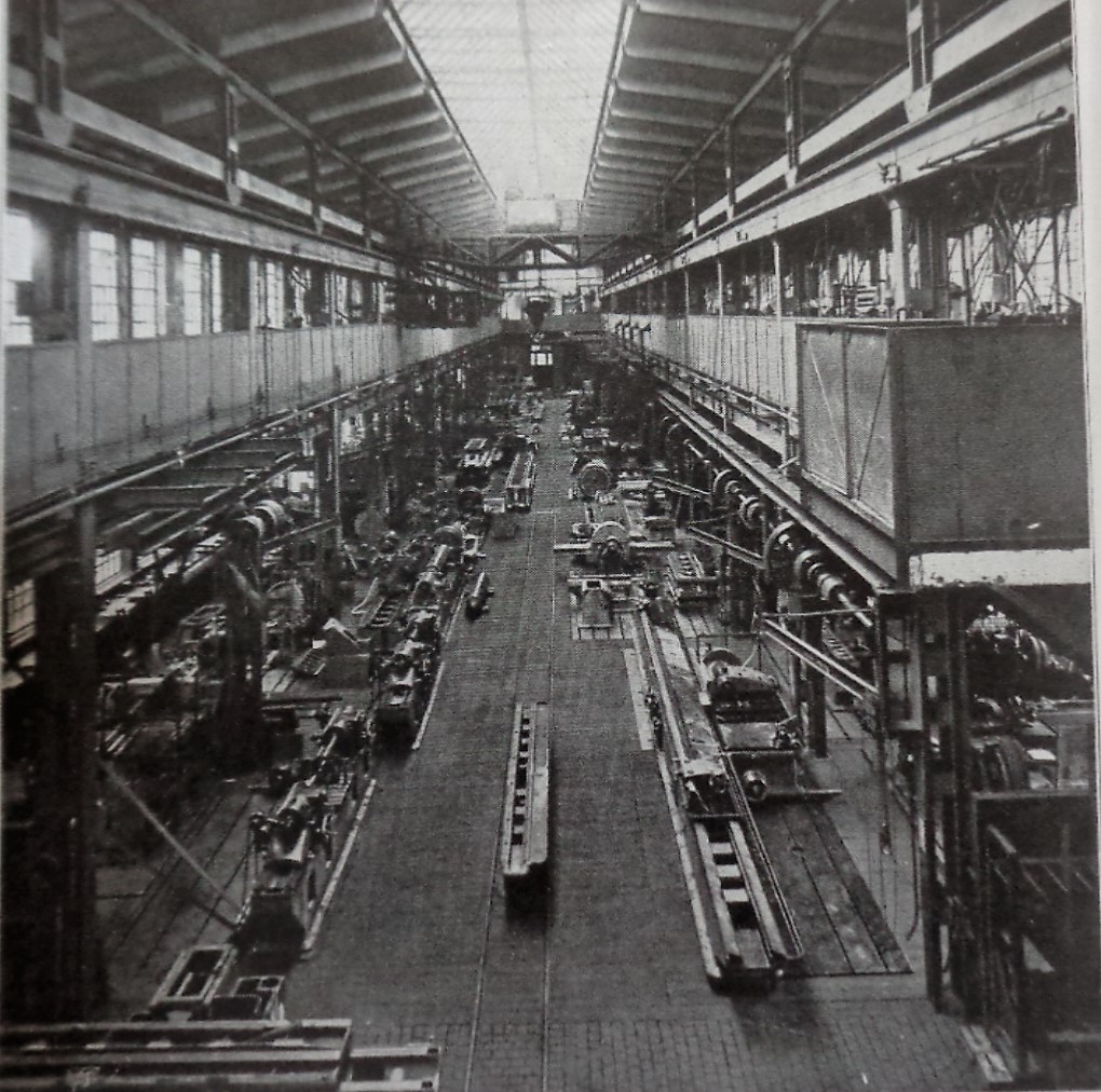 Schwarz-Weiß-Aufnahme der Naxoshalle Anfang des 20. Jahrhunderts, mit langen Werkbänken, Maschinen und einem hohen Glasdach.