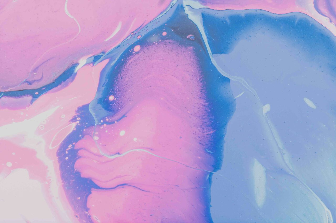 Das Bild zeigt eine abstrakte Komposition aus sanft verlaufenden Rosa-, Pink-, Violett- und Blautönen. Organische, fließende Formen erinnern an vermischte Tinte, Aquarellfarbe oder Marmorierungen. Im linken Bereich dominieren helle Rosatöne, während die rechte Seite überwiegend von zarten Blautönen geprägt ist. Zwischen den Farbflächen verlaufen geschwungene Linien und transparente Übergänge. Kleine helle Punkte und Blasenstrukturen sind über das Bild verteilt und verleihen der Oberfläche eine schimmernde, flüssige Wirkung. Das Motiv ist rein abstrakt und zeigt keine erkennbaren Personen, Tiere oder Gegenstände.